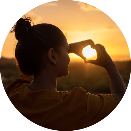 Woman making a heart shape around the setting sun
